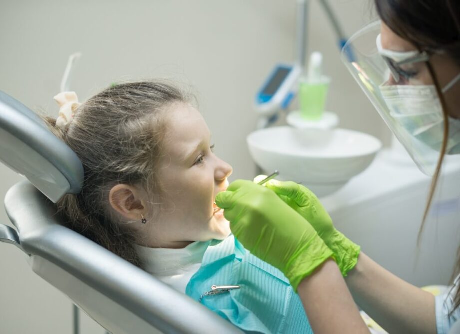 Dentystka pracuje z dzieckiem na fotelu dentystycznym, przypominając o różnicach między znieczuleniem ogólnym a podtlenkiem azotu stosowanym w stomatologii.