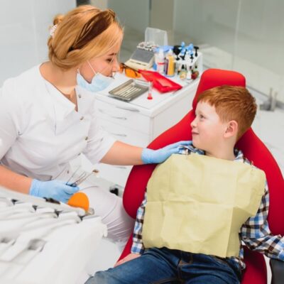 Dentystka udziela zalecenia po zabiegu stomatologicznym u dziecka, uśmiechając się do chłopca.