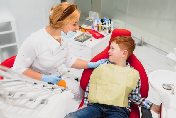 Dentystka udziela zalecenia po zabiegu stomatologicznym u dziecka, uśmiechając się do chłopca.