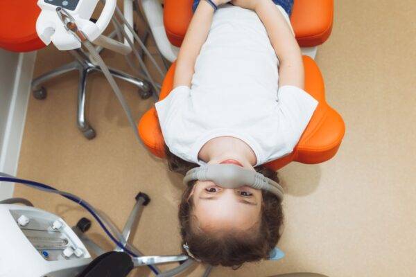 Dziewczynka w gabinecie dentystycznym korzysta z maski do inhalacji, co ilustruje działanie i bezpieczeństwo podtlenku azotu.